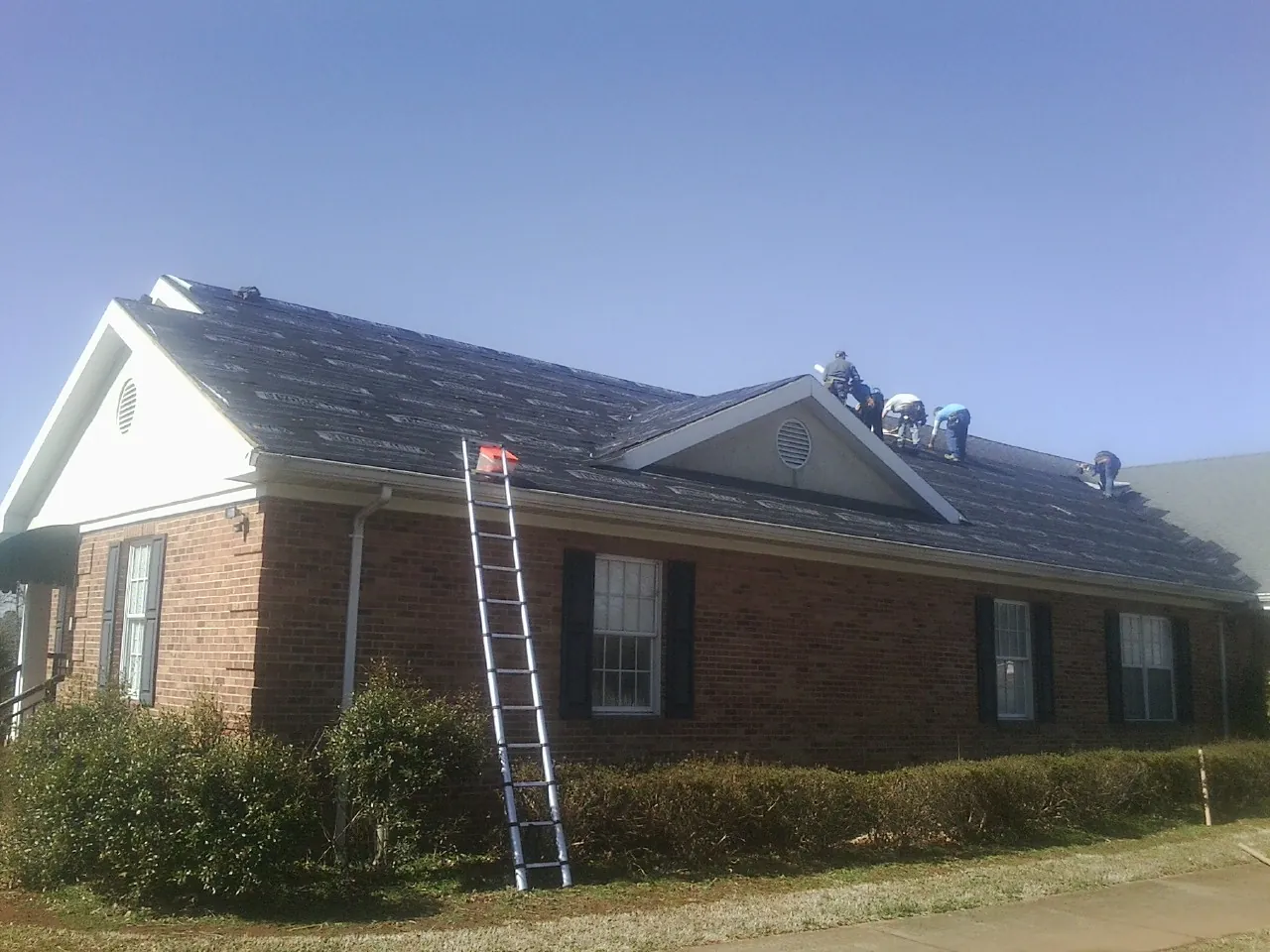 Crew tearing shingles off a brick ranch roof with a ladder set — Emergency Roof Repair work by our crew in Ford City