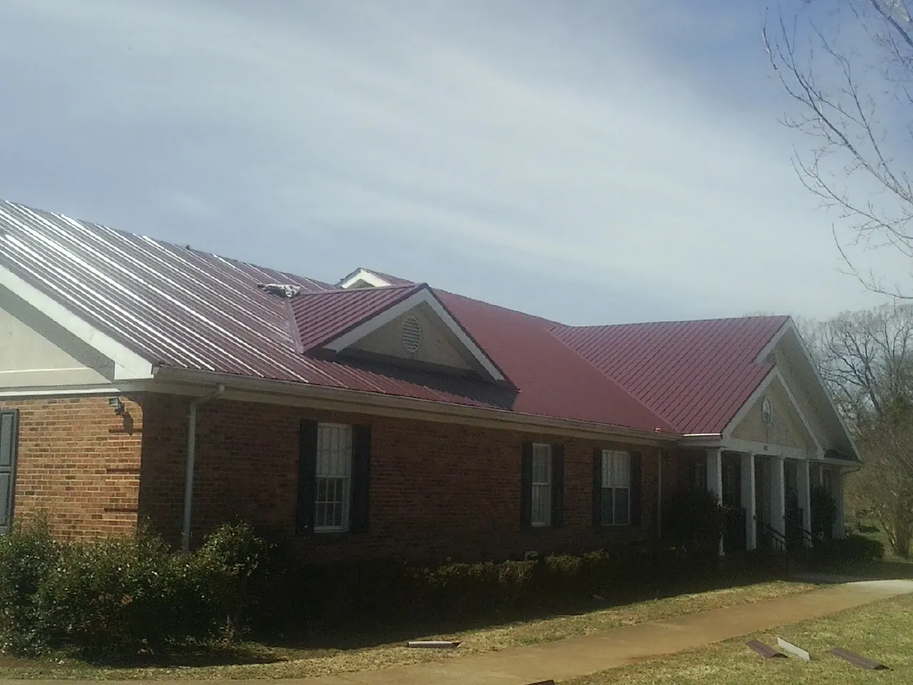 Red metal roof with gabled entries on a long brick building, from a Hail Damage Roof Repair job in Ford City