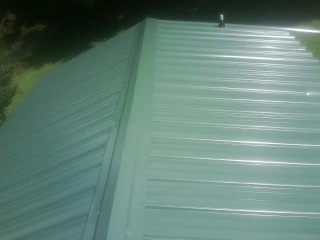 New green metal panels meeting at the ridge of a roof — Flat Roof Repair work by our crew in Ford City