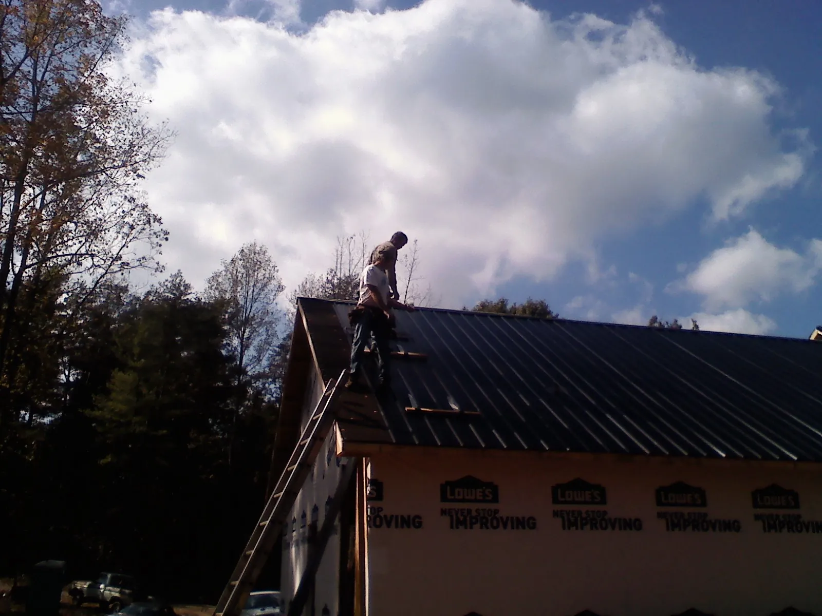 Roofer fastening dark metal panels high against a cloudy sky, from a Roof Inspection job in Ford City
