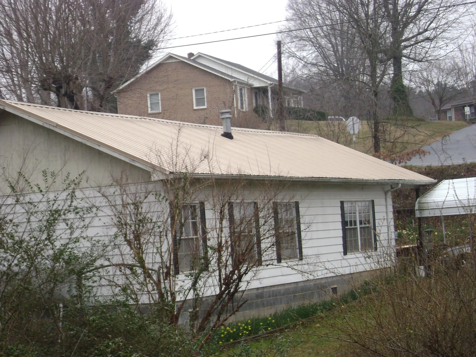 Tan metal roof on a white sided house set into a hillside — Commercial Roofing by Roofing Brothers in Ford City